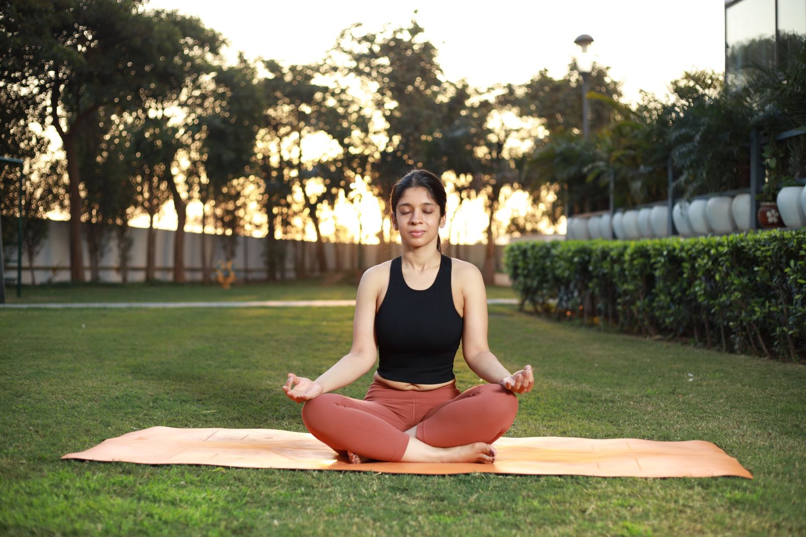 Juhie meditating cross-legged on a mat in a garden at sunset
