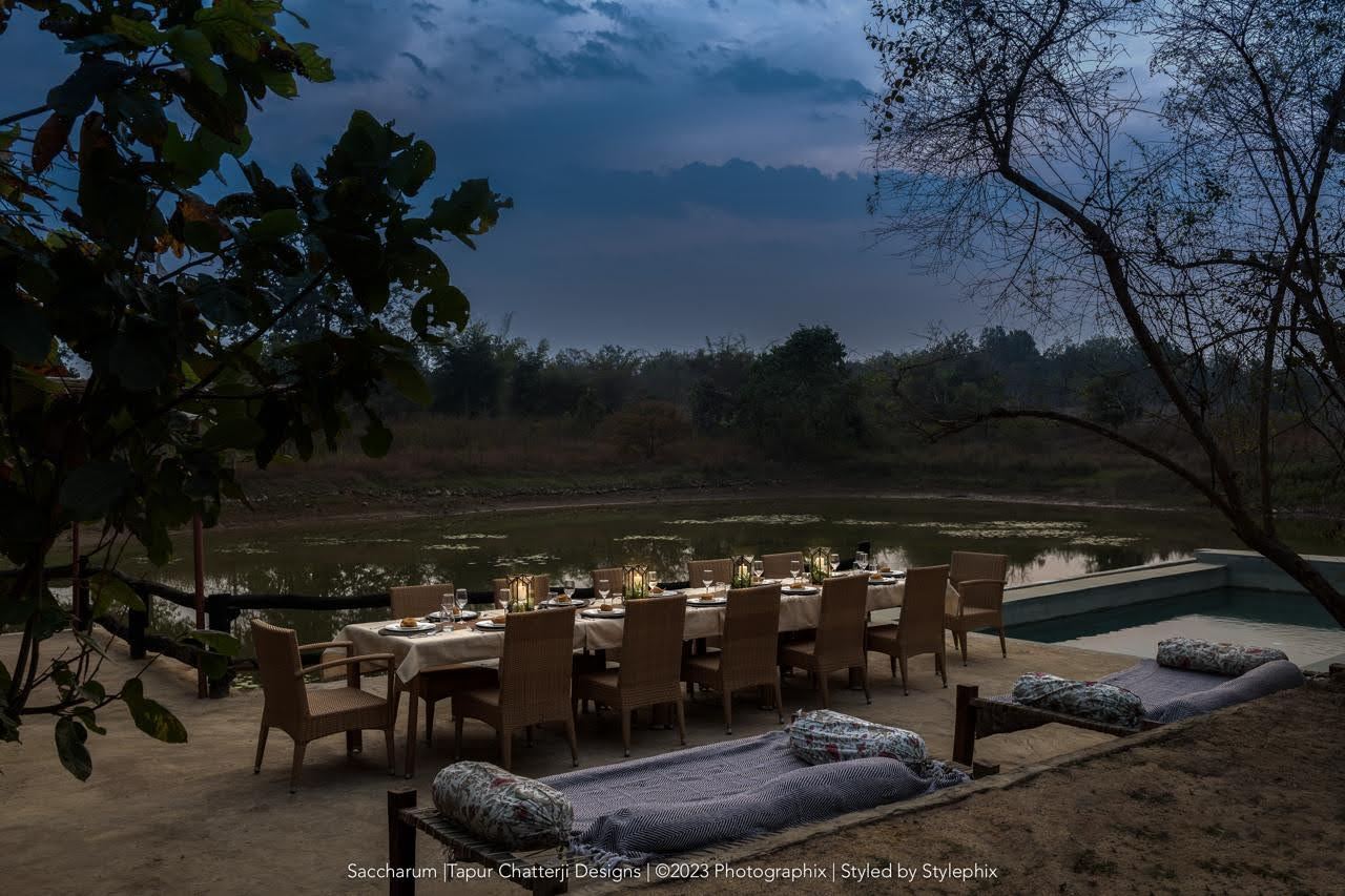 Candlelit dining table on a deck by the water at Saccharum Safari Lodge